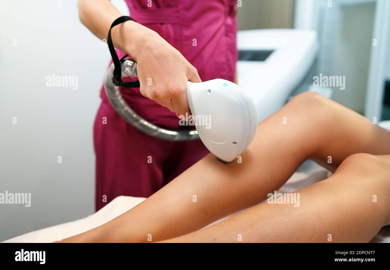 Laser-ipl-Gerät in der Hand der Kosmetikerin mit Lasermaschine am Bein des Kunden. Frau Körper Haarentfernung. Beintechnologie für die Kosmetologie Stockfoto