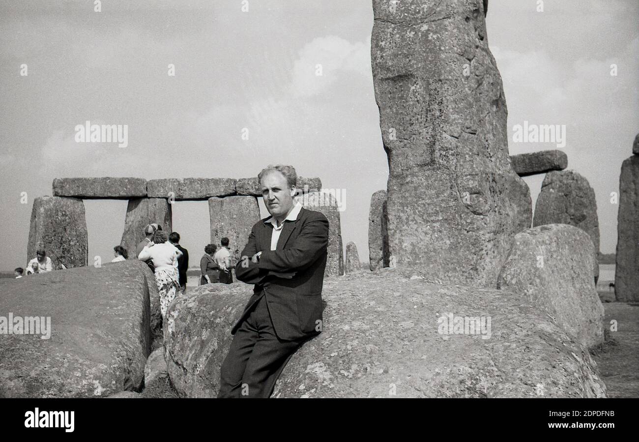 1950er Jahre, historisch, Menschen in Stonehenge, dem berühmten prähistorischen Denkmal auf der Salisbury Plain in Wiltshire, England, Großbritannien. Zu dieser Zeit konnten Besucher frei zwischen den alten Sarsensteinen spazieren gehen und - wie ein Mann hier sieht - auf ihnen sitzen, ohne Probleme, was später nicht erlaubt war. Stockfoto