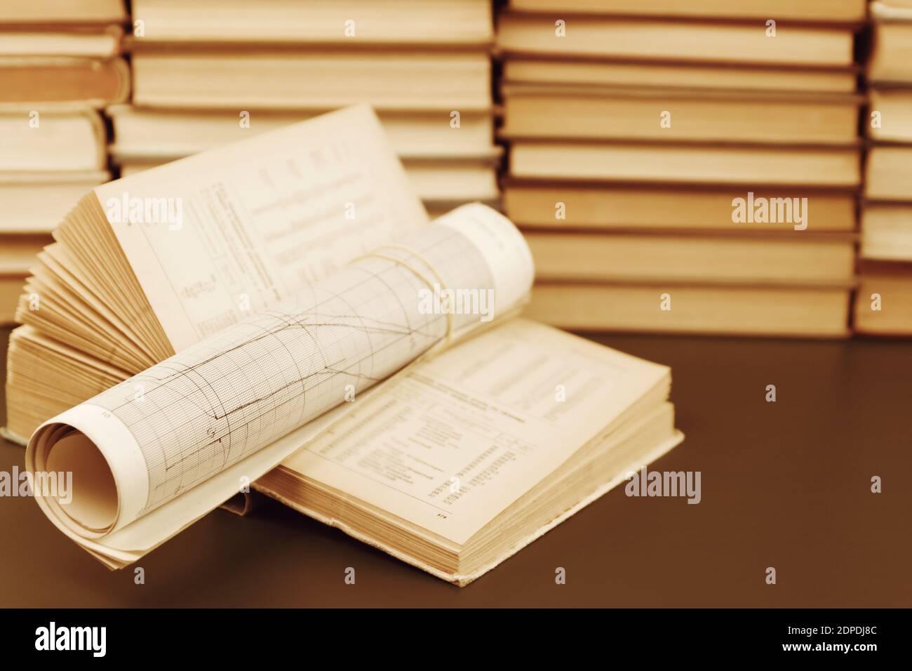 Wissenschaftliche Studie. Ein offenes Buch mit Referenztabellen und den Grafiken auf dem Schreibtisch auf dem Hintergrund eines Regals mit Büchern Stockfoto