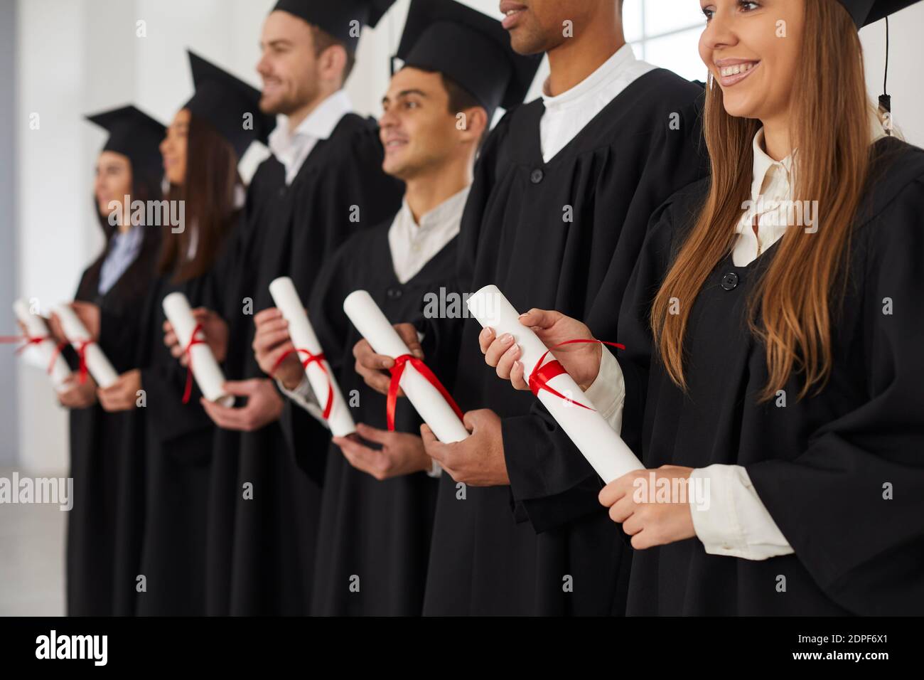 Gruppe von multiethnischen Menschen, die in einer Reihe stehen und Rollen von Diplomen in den Händen halten. Stockfoto