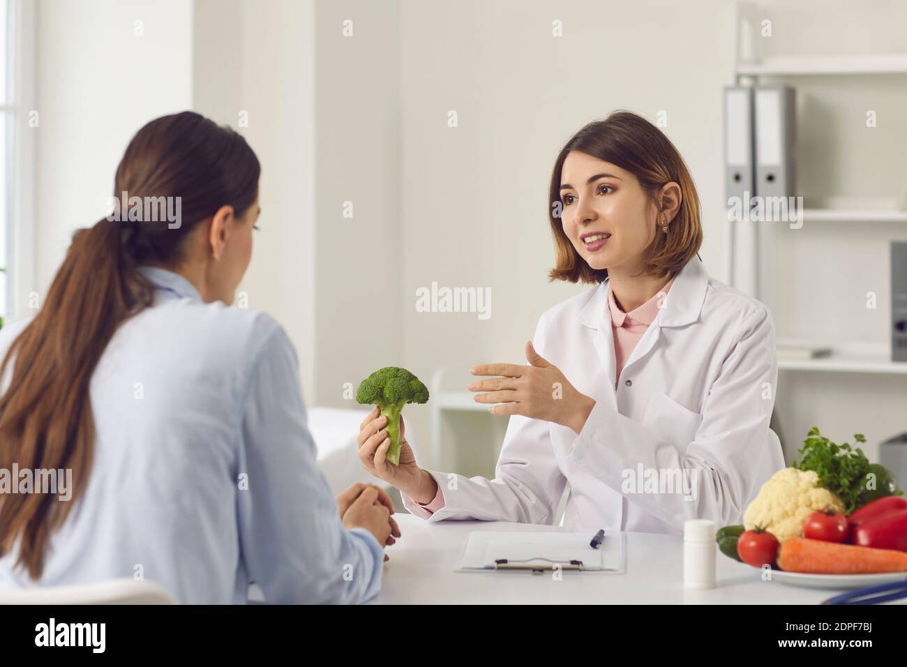 Ernährungsberater hält Brokkoli und erzählt junge Frau über die Vorteile der Gesunde Ernährung Stockfoto