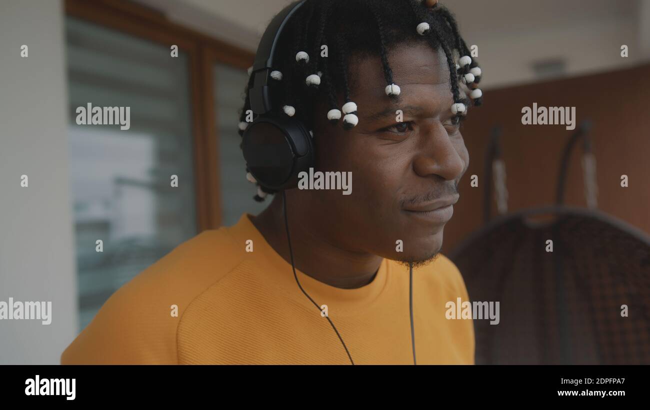 Porträt eines afroamerikanischen schwarzen Mannes mit Dreadlocks, der die Musik auf dem Balkon mit dem Headset hört. Hochwertige Fotos Stockfoto