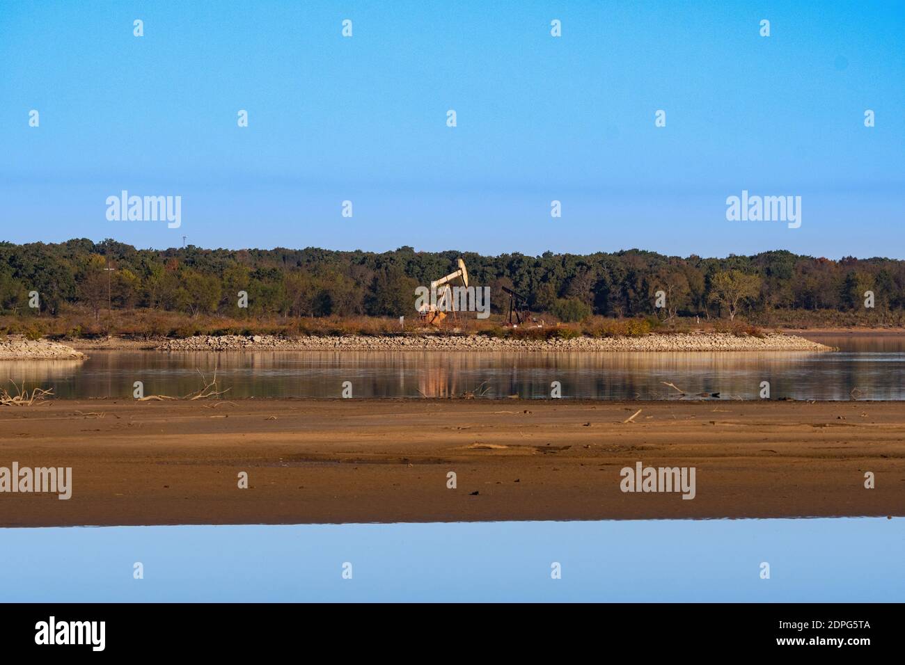 Ölpumpenheber auf einer felsigen Halbinsel, die an einem sonnigen Morgen in das seichte Wasser eines Sees hinausragt. Stockfoto