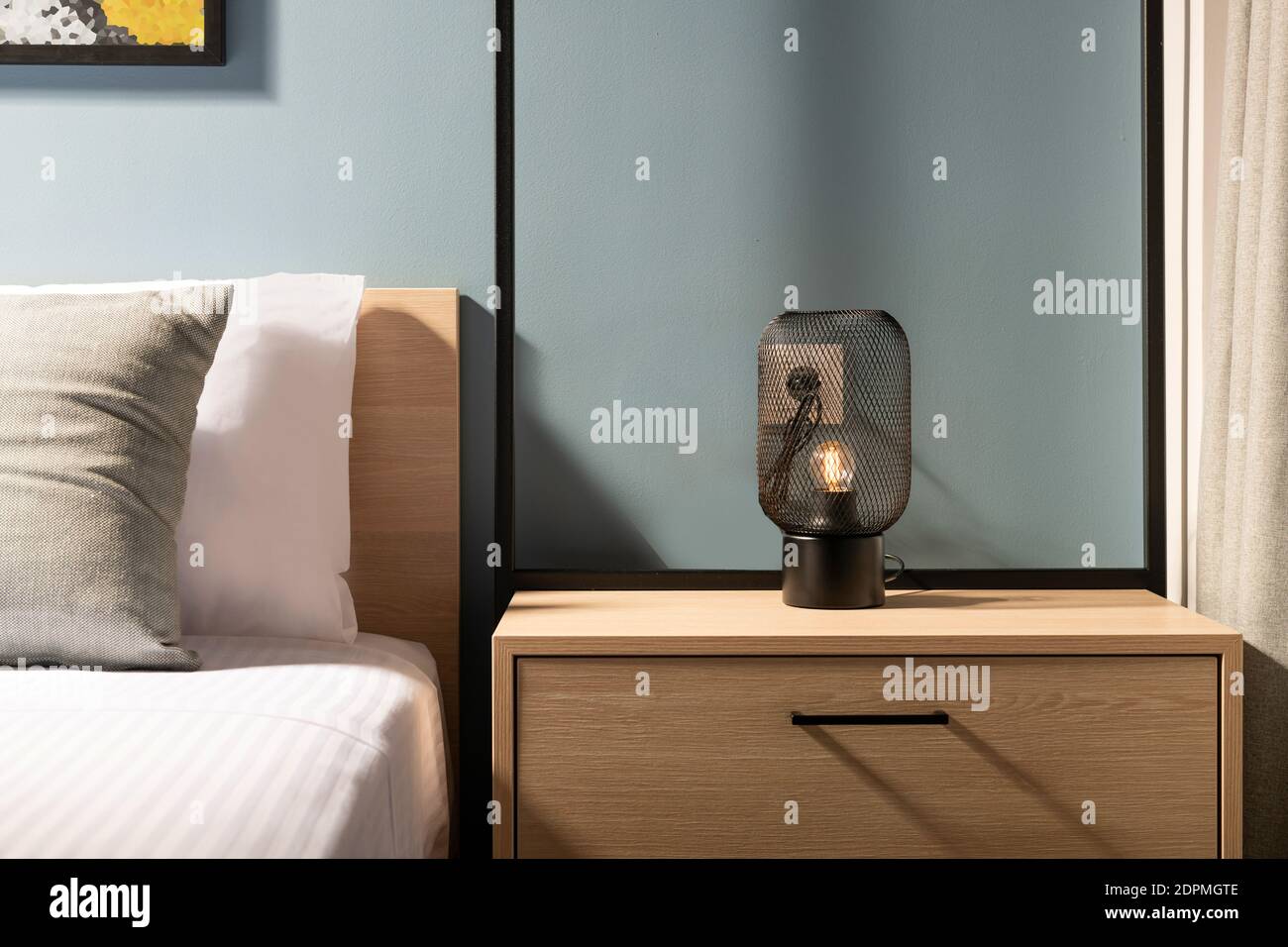 Nahaufnahme der modernen schwarzen Metall edison Lampe auf Holz Nachttisch im Schlafzimmer in zeitgenössischem Stil mit grauer Zimmereinrichtung Bett aus Kiefernholz und weißes Kinderbett Stockfoto