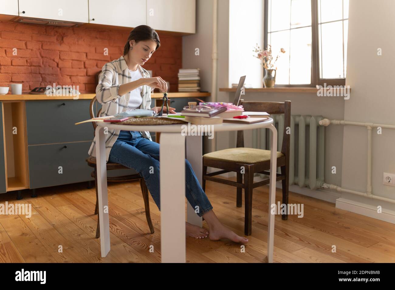 Fokussierte Studentin in Heimkleidung Zeichnung mit Trennwerkzeug Beim Sitzen am Küchentisch zu Hause Stockfoto