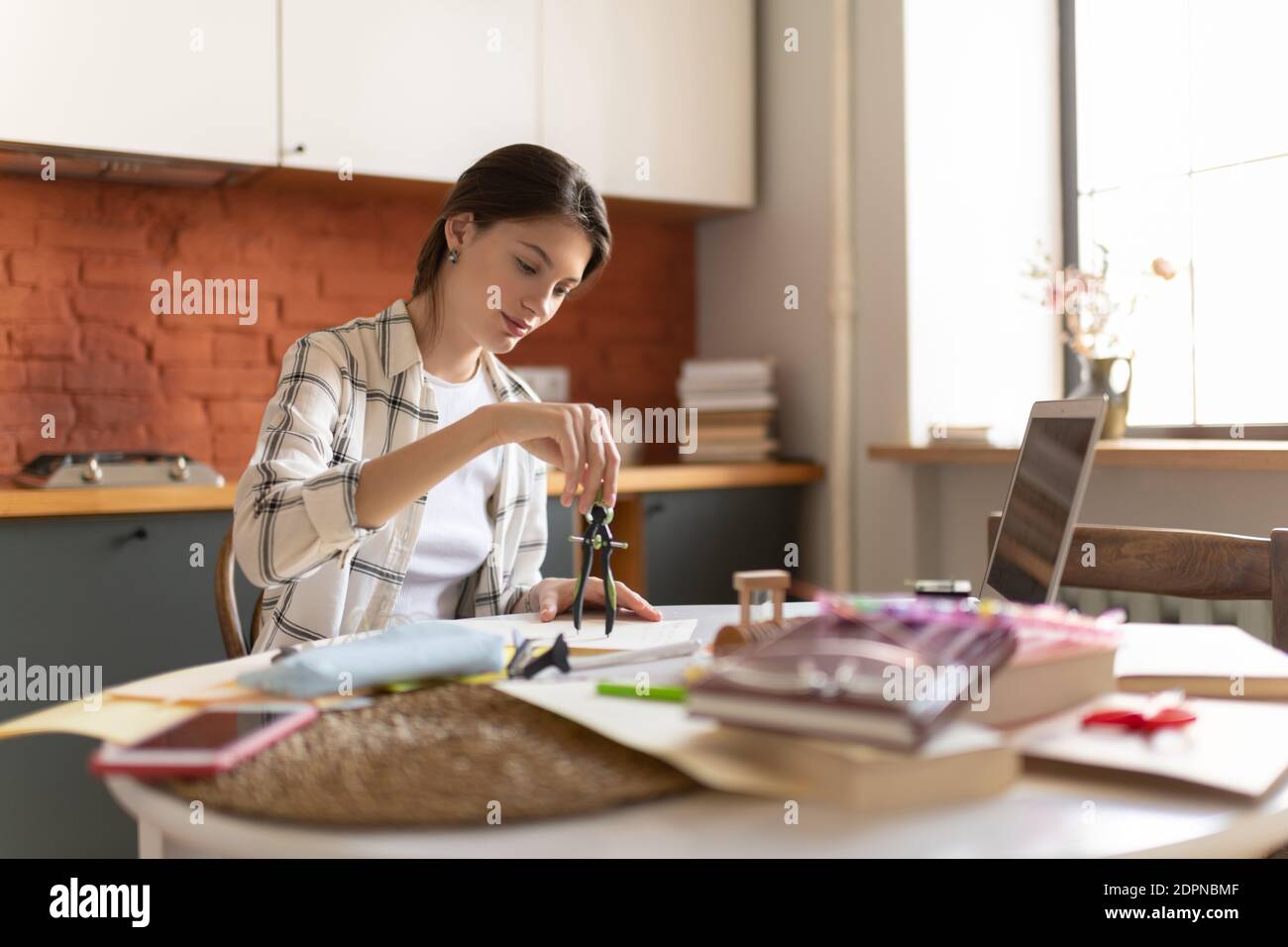 Junge Frau mit Trennwerkzeug beim Zeichnen Entwurf für Hochschule Aufgabe sitzen am Tisch in der Küche Stockfoto