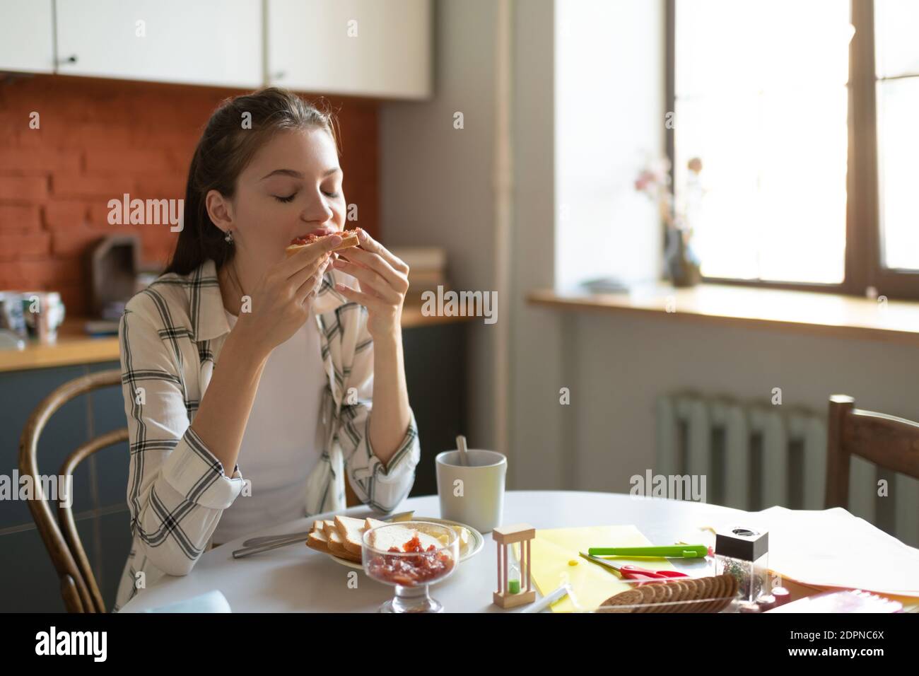 Schöne Teenager-Mädchen essen Sandwich mit Vergnügen zum Frühstück vor Schule in der Küche am Morgen Stockfoto
