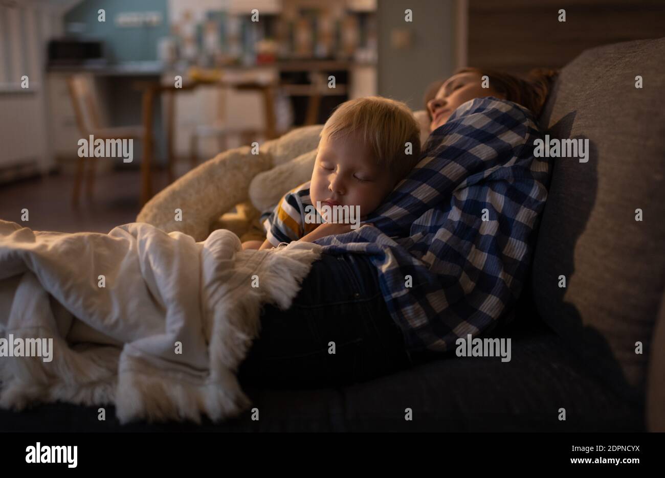 Ruhiges blondes kleines männliches Kind, das in den Armen einschläft Von jungen Schwester in Freizeitkleidung auf bequemen Sofa an Wohnzimmer Stockfoto