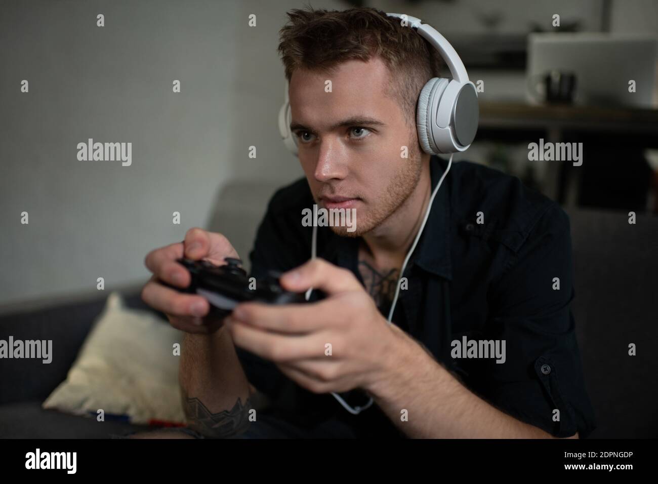 Konzentrierter junger Mann in Kopfhörern mit Controller, um Video zu spielen Spiel, während Sie zu Hause auf der Couch sitzen Stockfoto