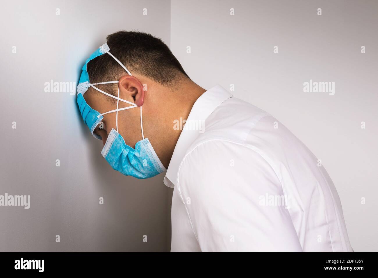 Ein Mann mit medizinischen Einwegmasken lehnte seinen Kopf gegen die Wand. Konzept zur Depression aufgrund von Quarantäne durch COVID-19 Pandemie verursacht. Stockfoto