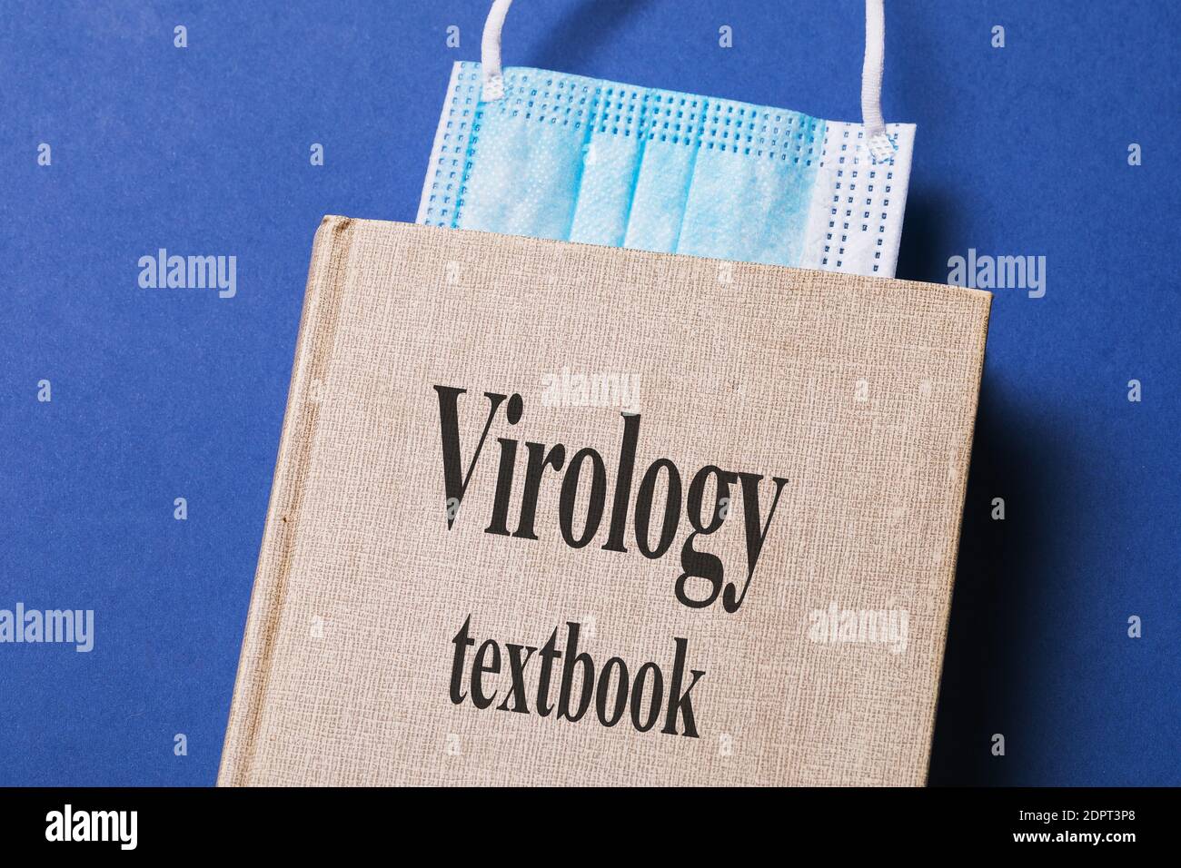 Virologisches Lehrbuch mit einem Lesezeichen aus einer medizinischen Maske auf dem Tisch. Stockfoto