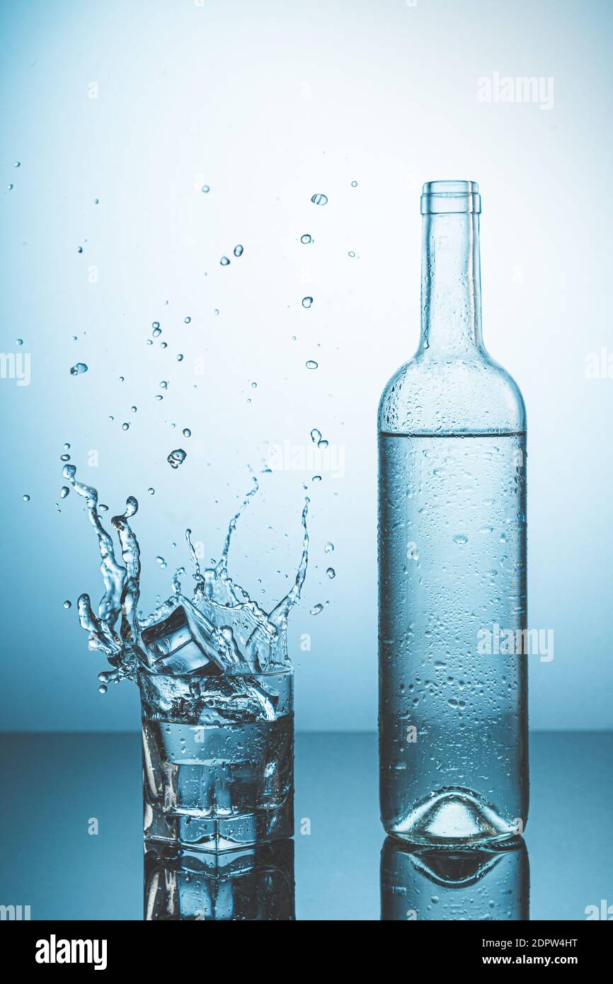 Flasche Eiswasser mit Tropfen, und Glas Wasser mit Eis fallen mit Spritzer. Wasserspritzer und erfrischende Getränke Konzept. Stockfoto