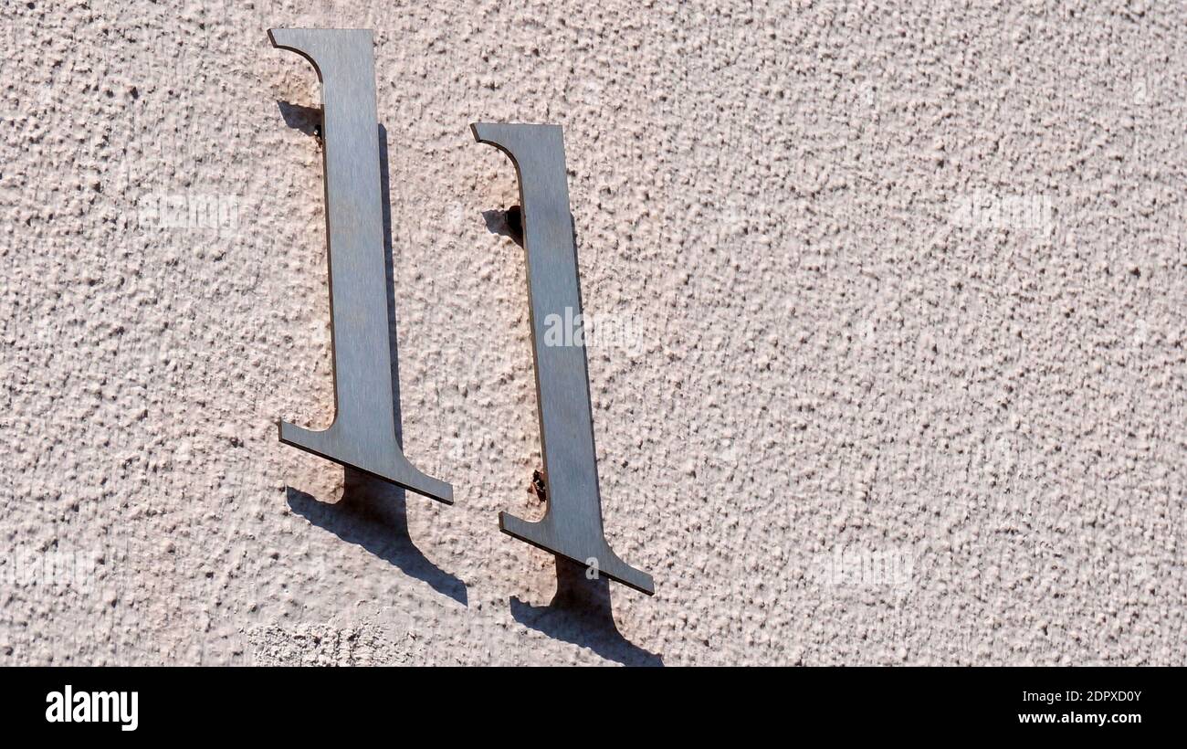 Eine weiße Mauer und Hausnummer 11 und der Schatten dieser Zahl an der Wand Stockfoto