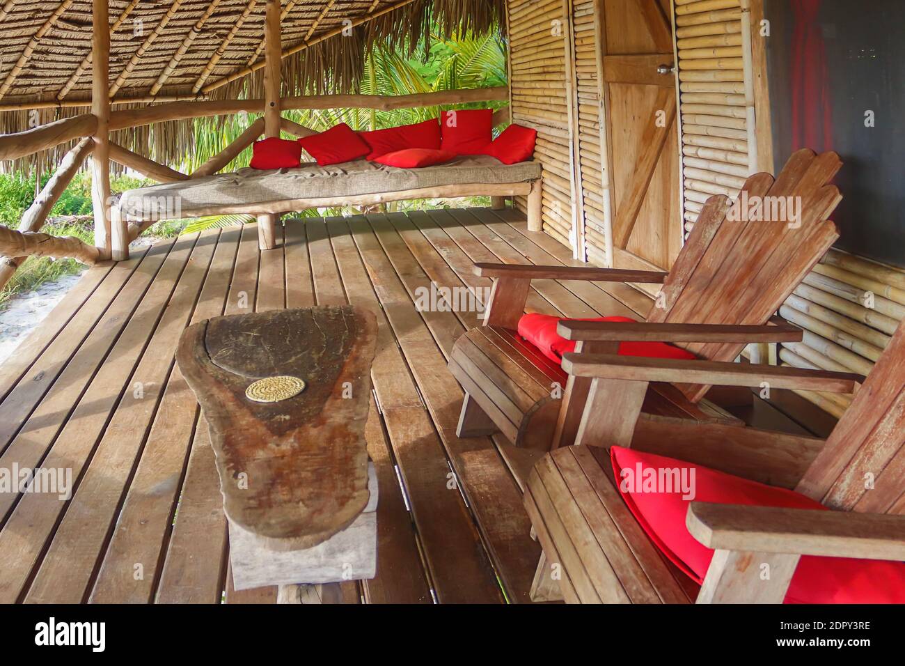 Ökologisches Haus, die Dschungelvilla aus Bambus und lokalen Materialien, komfortable Holzstühle und massiver Tisch auf Balkon mit roten Kissen Stockfoto