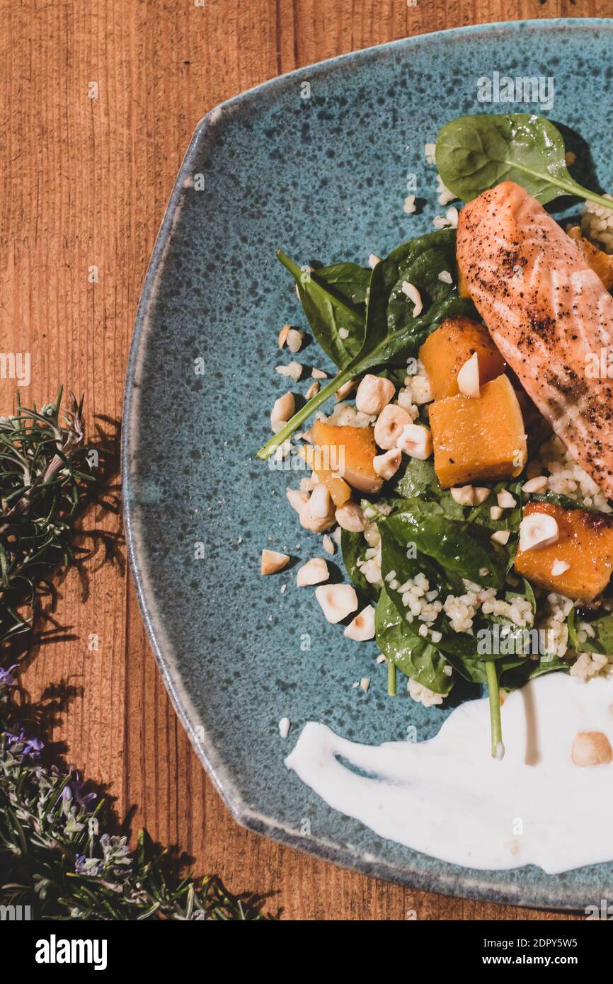 Typischer Fisch frischer Teller, leckerer gegrillter Lachs mit gegrillten Kürbissen und Joghurtsauce auf einem schicken Holztisch. Mediterrane Gerichte mit einem Stockfoto