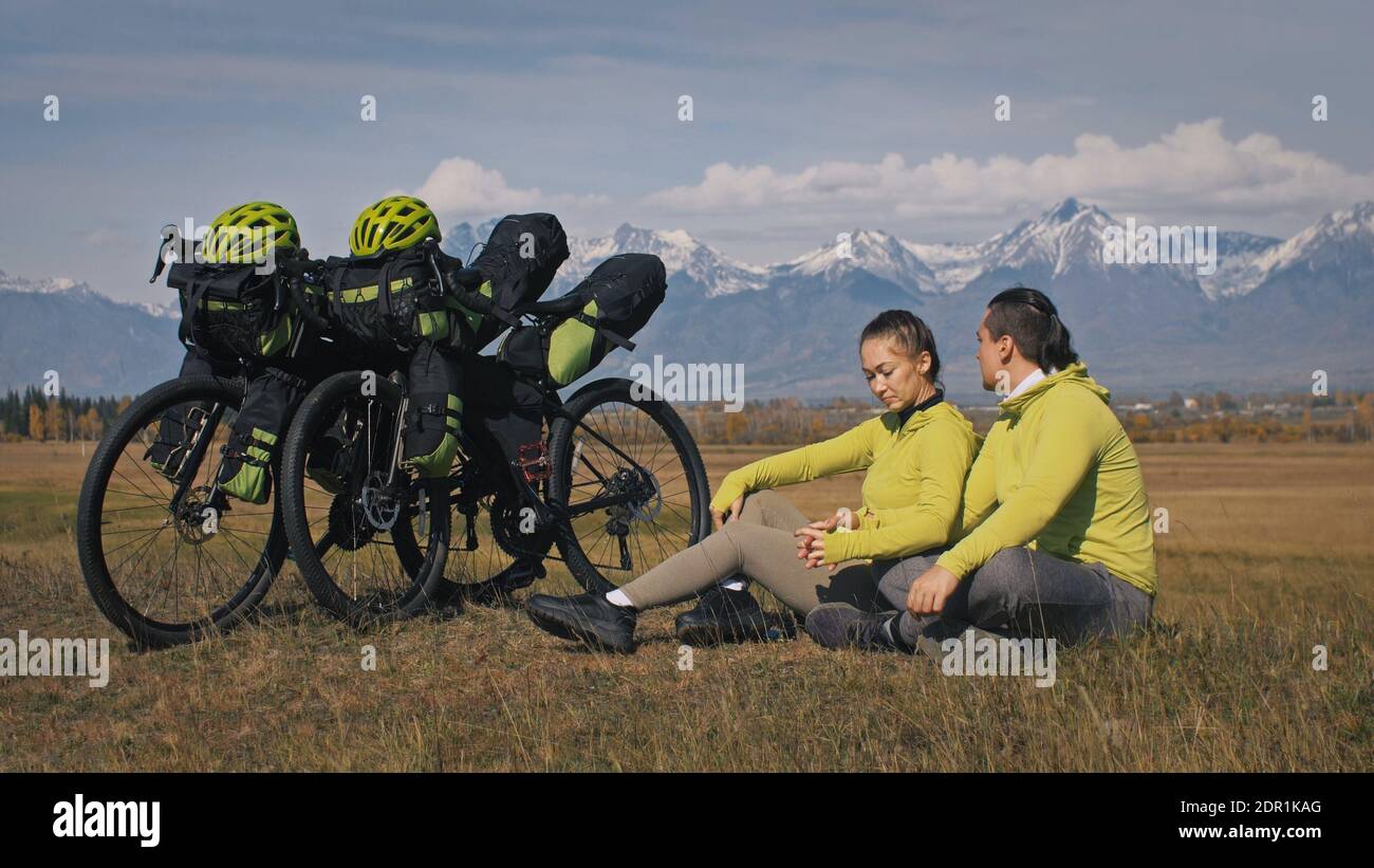 Der Mann und die Frau reisen auf gemischtem Terrain mit Bikepacking. Die beiden Personen reisen mit Fahrradtaschen. Schneebedeckte Berge. Stockfoto