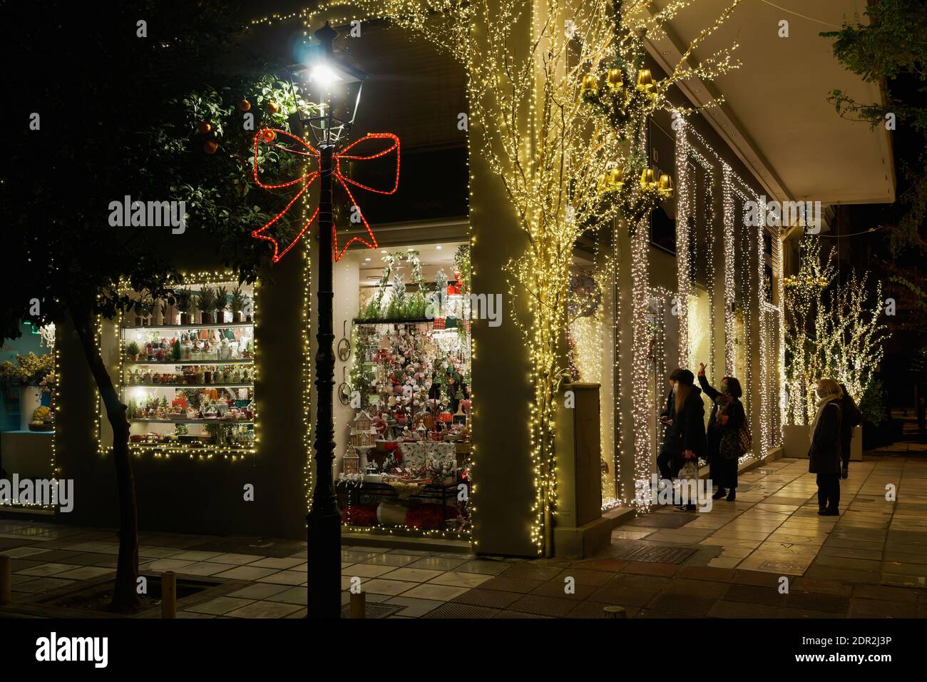 Thessaloniki, Griechenland - Dezember 18 2020: Hellenic Weihnachtsgeschäft mit Kunden warten auf den Eingang.Menge in der Schlange außerhalb beleuchtet Nacht Blick auf dekorierten saisonalen Speicher. Stockfoto