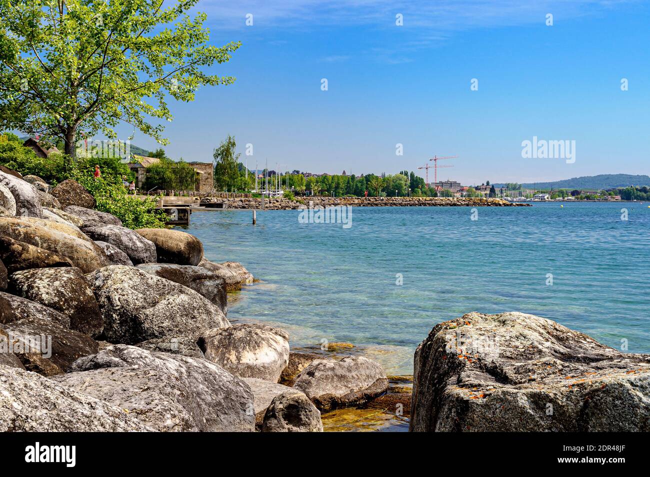 Ufer des Sees Neuchâtel. Sehr schönes sonniges Wetter. Seltene Wolken von schönem Wetter am blauen Himmel. Ein Pier schneidet die Landschaft. Im Vordergrund. Stockfoto