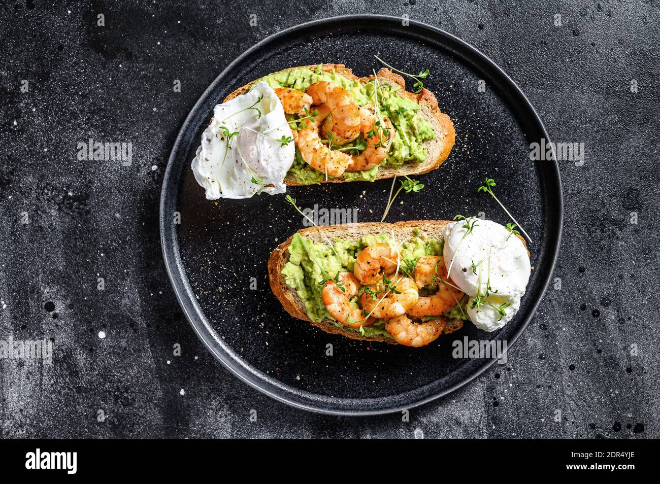 Toast mit Garnelen, Garnelen, Avocado und pochiertem Ei. Schwarzer Hintergrund. Draufsicht. Stockfoto