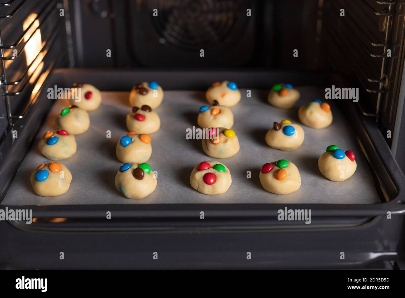 Backblech im Ofen mit ungekochten Plätzchen. Hausgemachte Kekse mit farbigen Süßigkeiten. Stockfoto