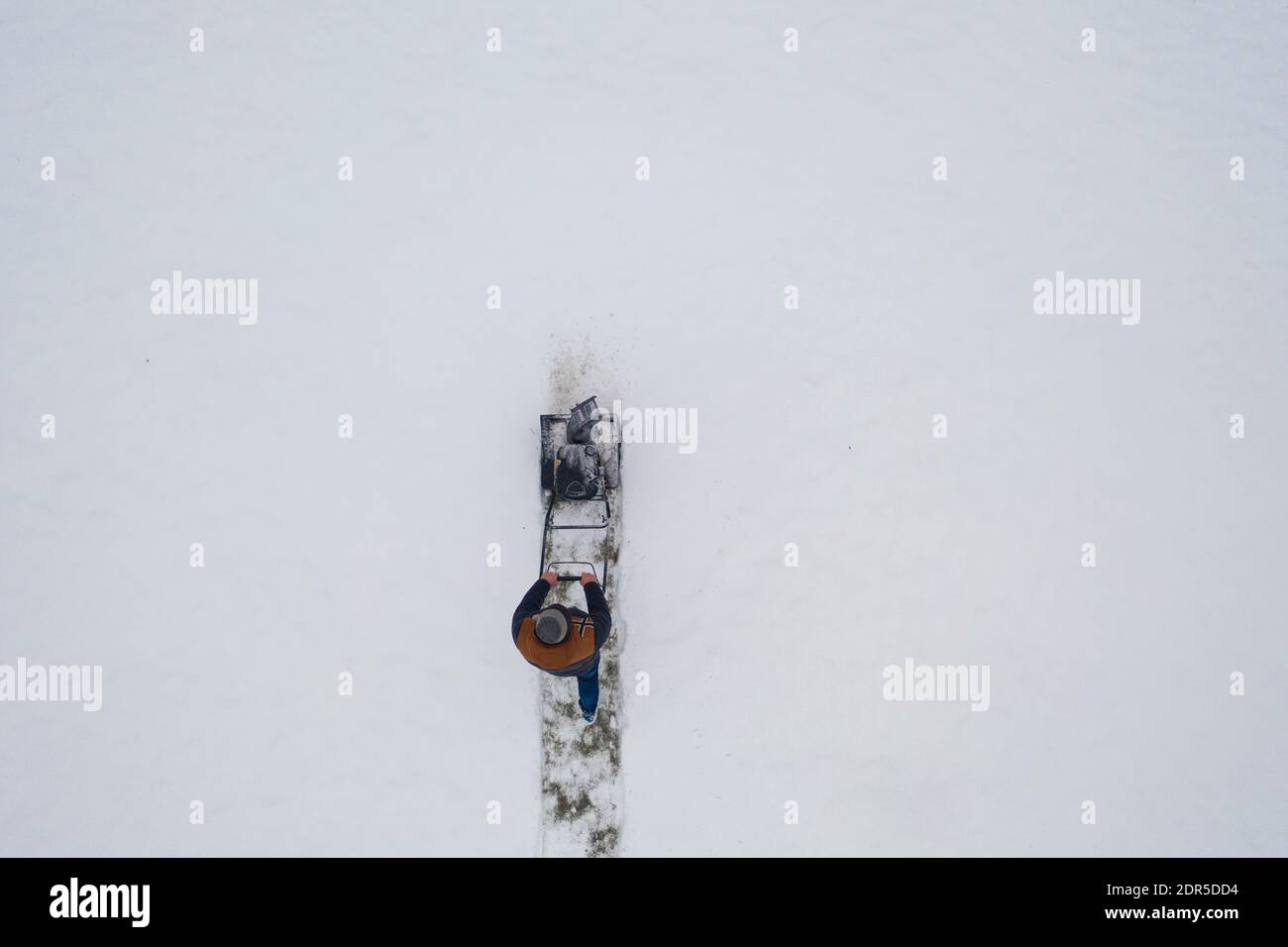 Luftaufnahme Schneefräse bei der Arbeit an einem Wintertag. Mann, der nach Schneefall Schnee entfernt. Gärtner beim Abräumen des Eises. Draufsicht Schneefräse wird geräumt Stockfoto