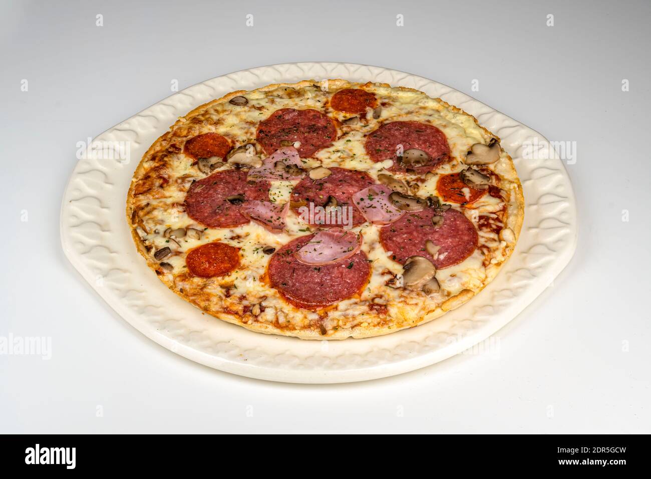 Eine fertig gebackene Pizza mit Salami, Schinken und Käse liegt auf einem runden Teller. Stockfoto