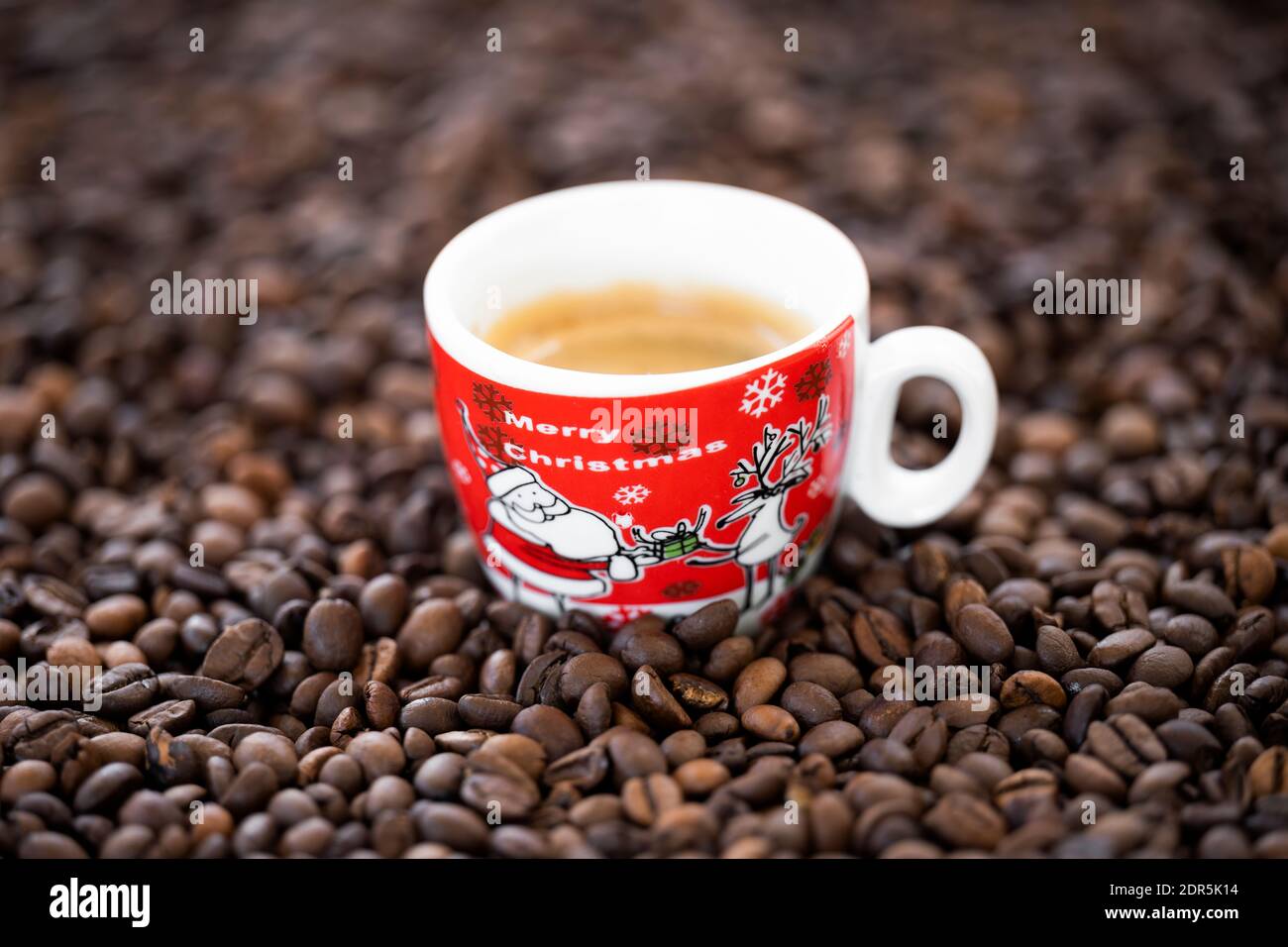 Flache Lay mit Kopierraum, (selektiver Fokus) EINE Weihnachtstasse mit etwas cremigem Kaffee wird auf einige geröstete Kaffeebohnen gelegt. Stockfoto