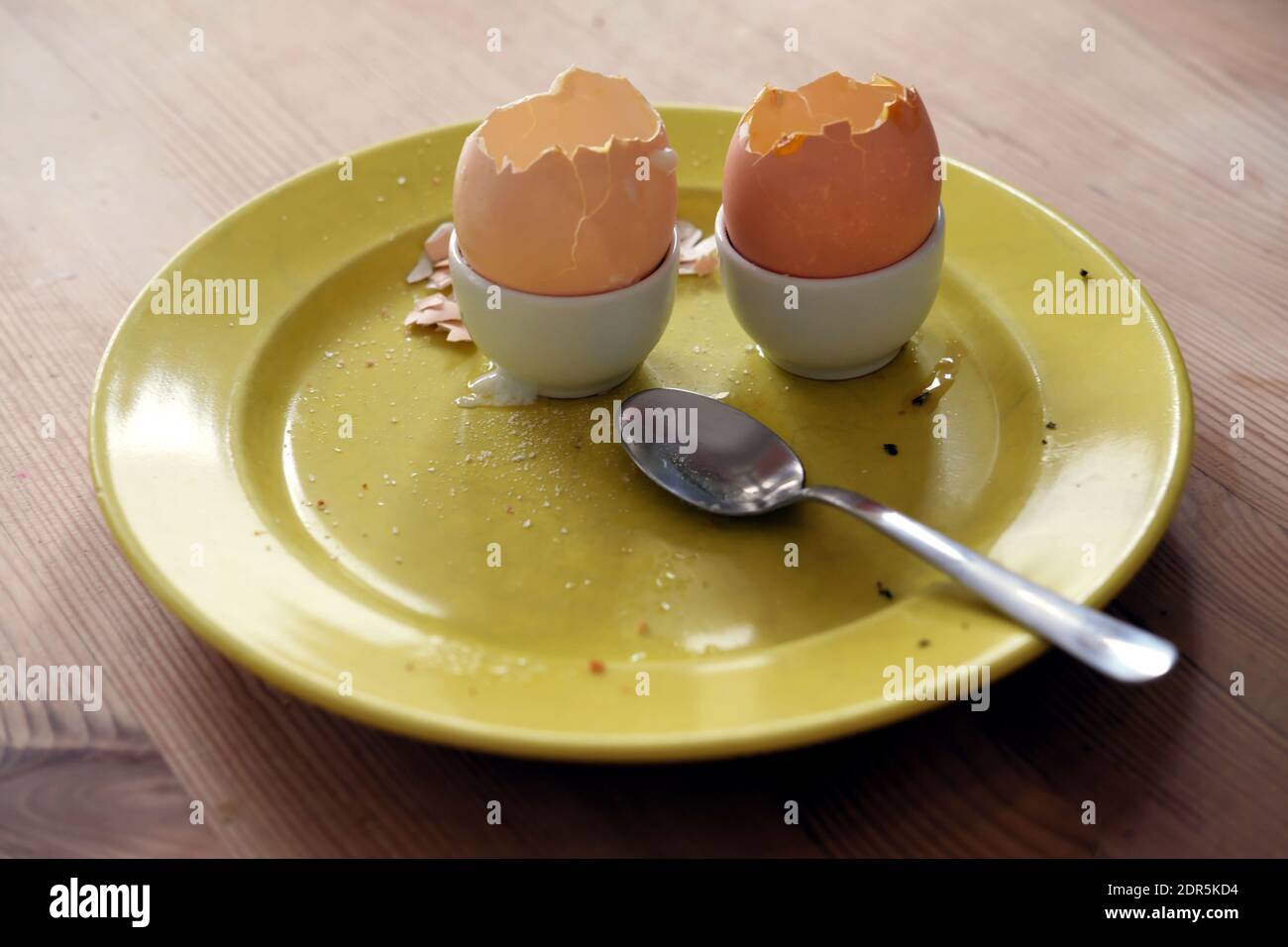 Nach dem Frühstück - gelbe Platte mit rissigen, leeren Eierschalen und einem Löffel auf einem Holztisch nach dem Essen gelassen Stockfoto