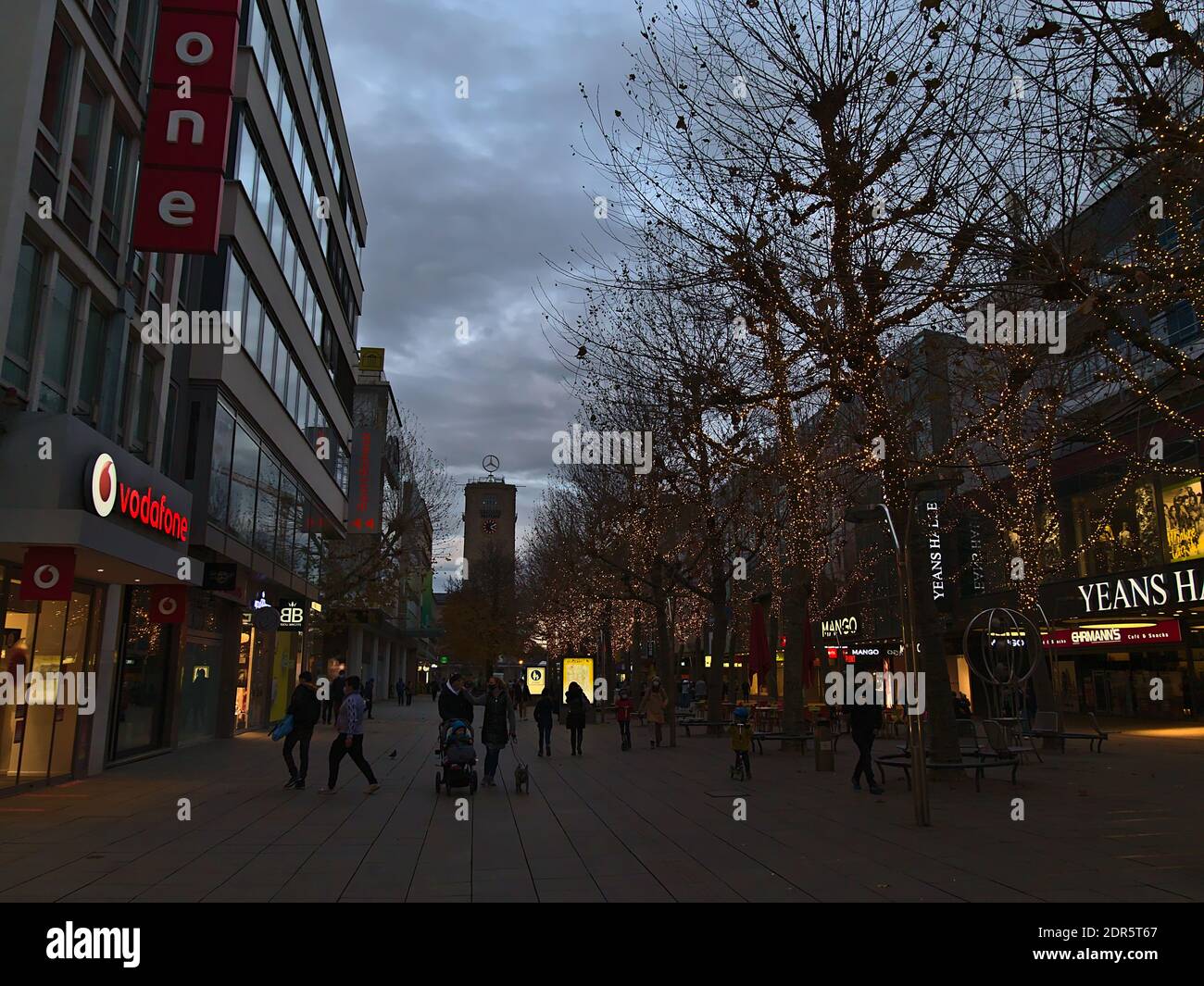 Menschen mit Gesichtsmasken wandern in der beliebten Einkaufsstraße Königstraße in der Innenstadt in der Weihnachtszeit mit geschmückten Bäumen und Turm des Hauptbahnhofs. Stockfoto