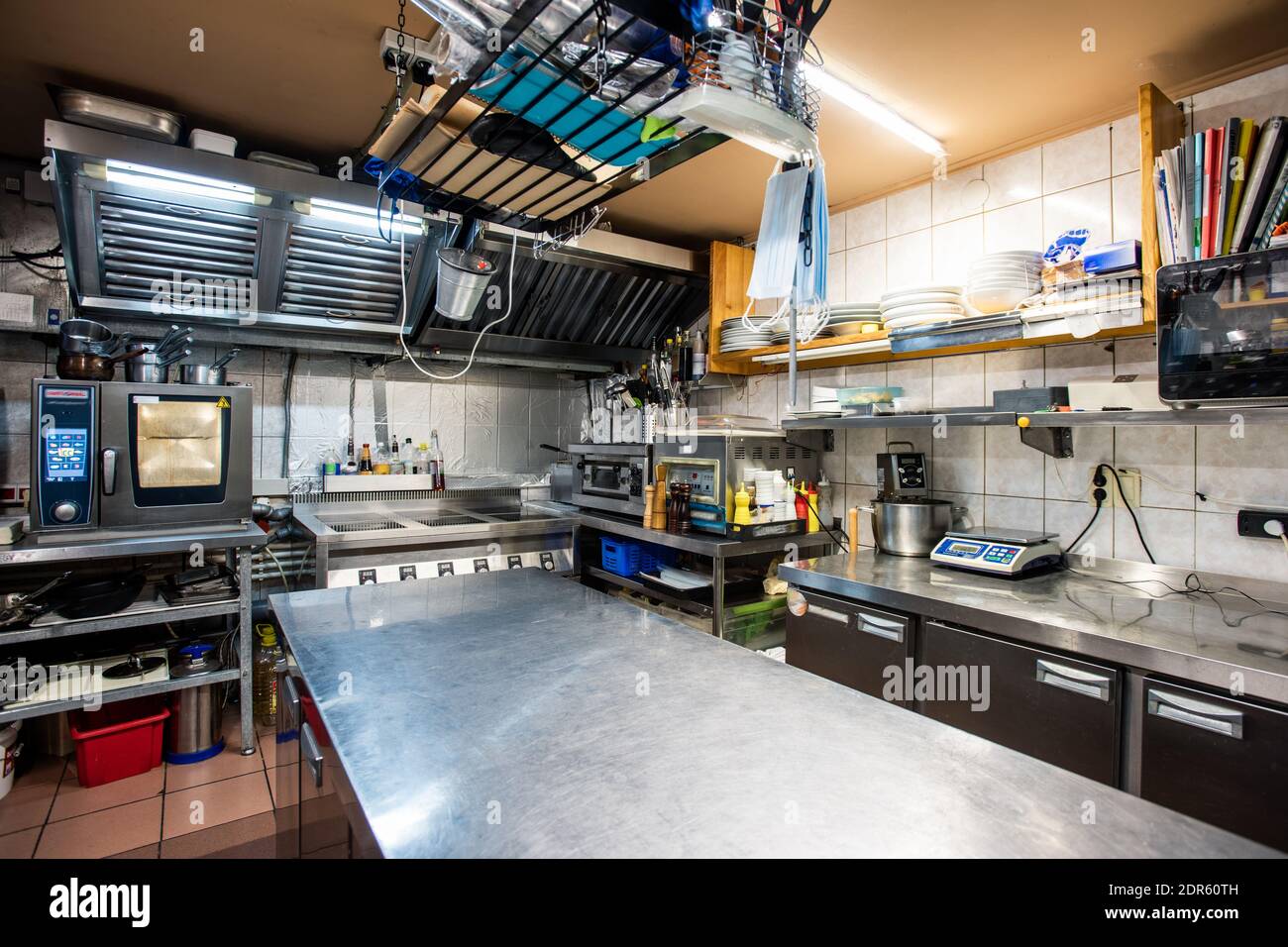 Interieur der großen Küche des modernen Restaurants mit großem Tisch zum Kochen, Geschirr, Regale, Elektroherd, Backofen und andere Geräte Stockfoto