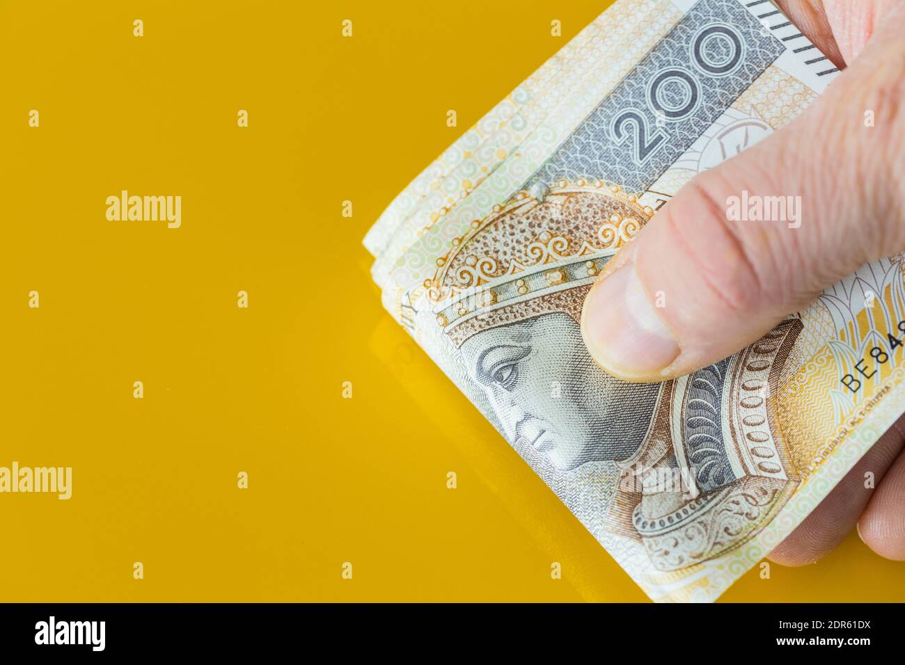 Ein Bündel polnisches Geld, zweihundert Zloty-Banknoten, in Händen gehalten. Gelber Hintergrund mit Platz für Text Stockfoto