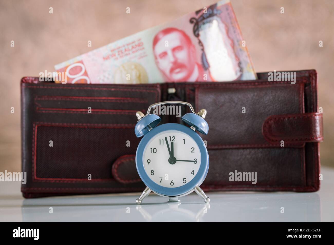 Stilvoller Wecker für fünf bis zwölf Personen. Im Hintergrund eine Brieftasche mit einem klebenden Haufen neuseeländischen Geldes. Hundert Dollarscheine Stockfoto