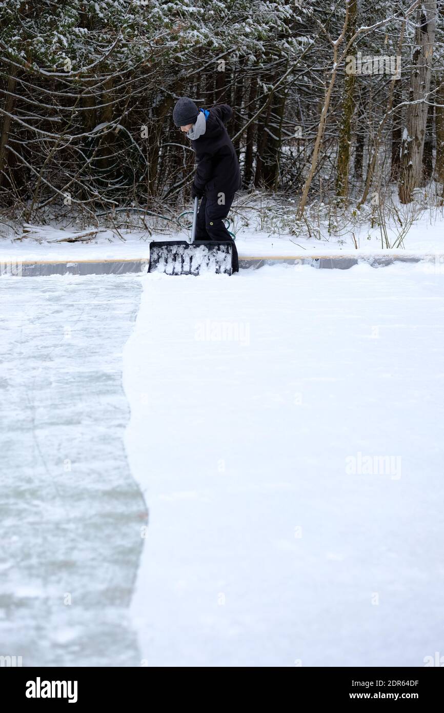 Ein junger Mensch, der im Winter in Ottawa, Ontario, Kanada Schnee von einer Eisbahn entfernt. Stockfoto