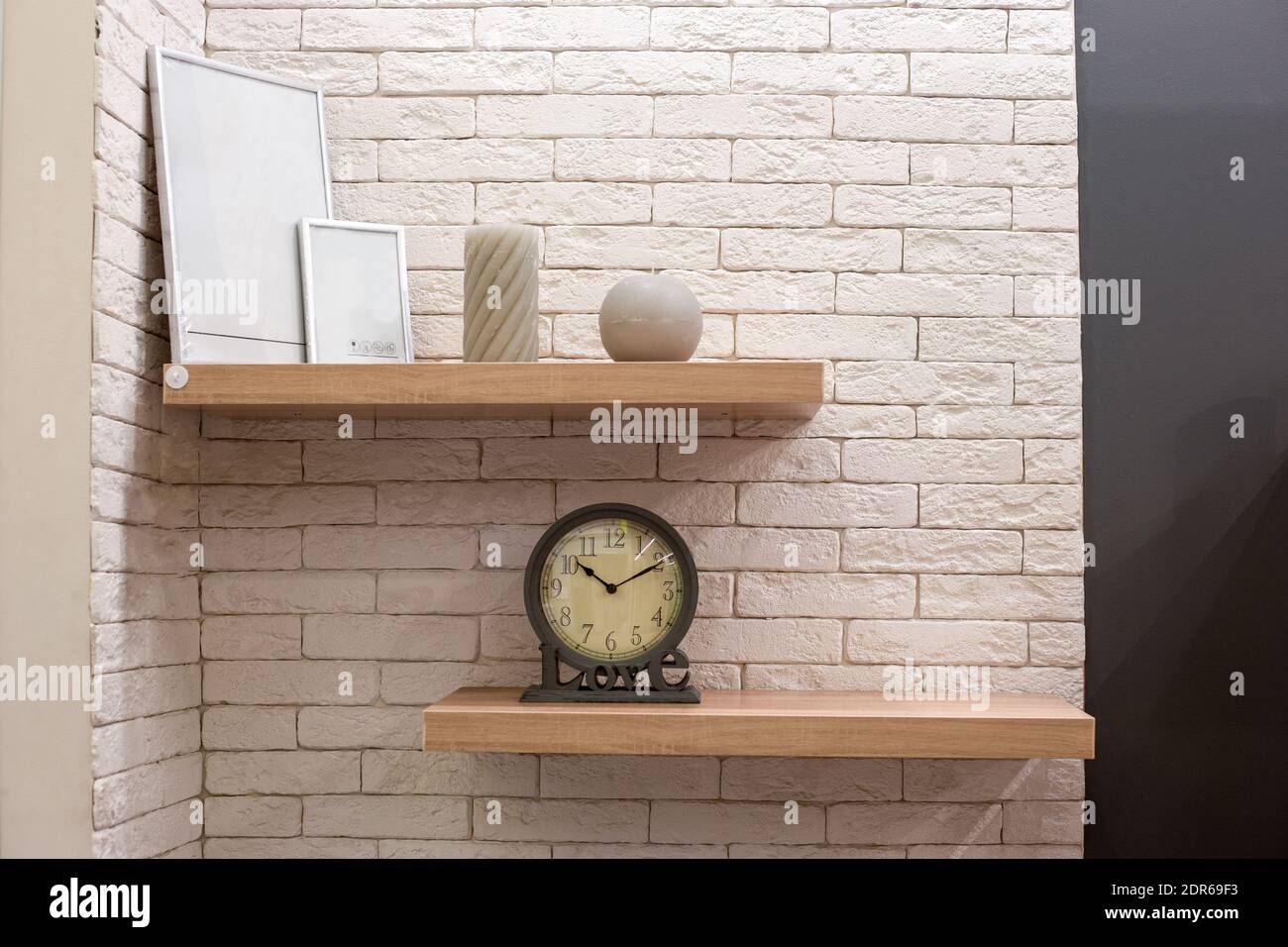Innenarchitektur des Zimmers. Holzregale mit Bilderrahmen, Kerzen und eine Uhr gegen eine leichte Ziegelwand. Hausreparaturen Stockfoto