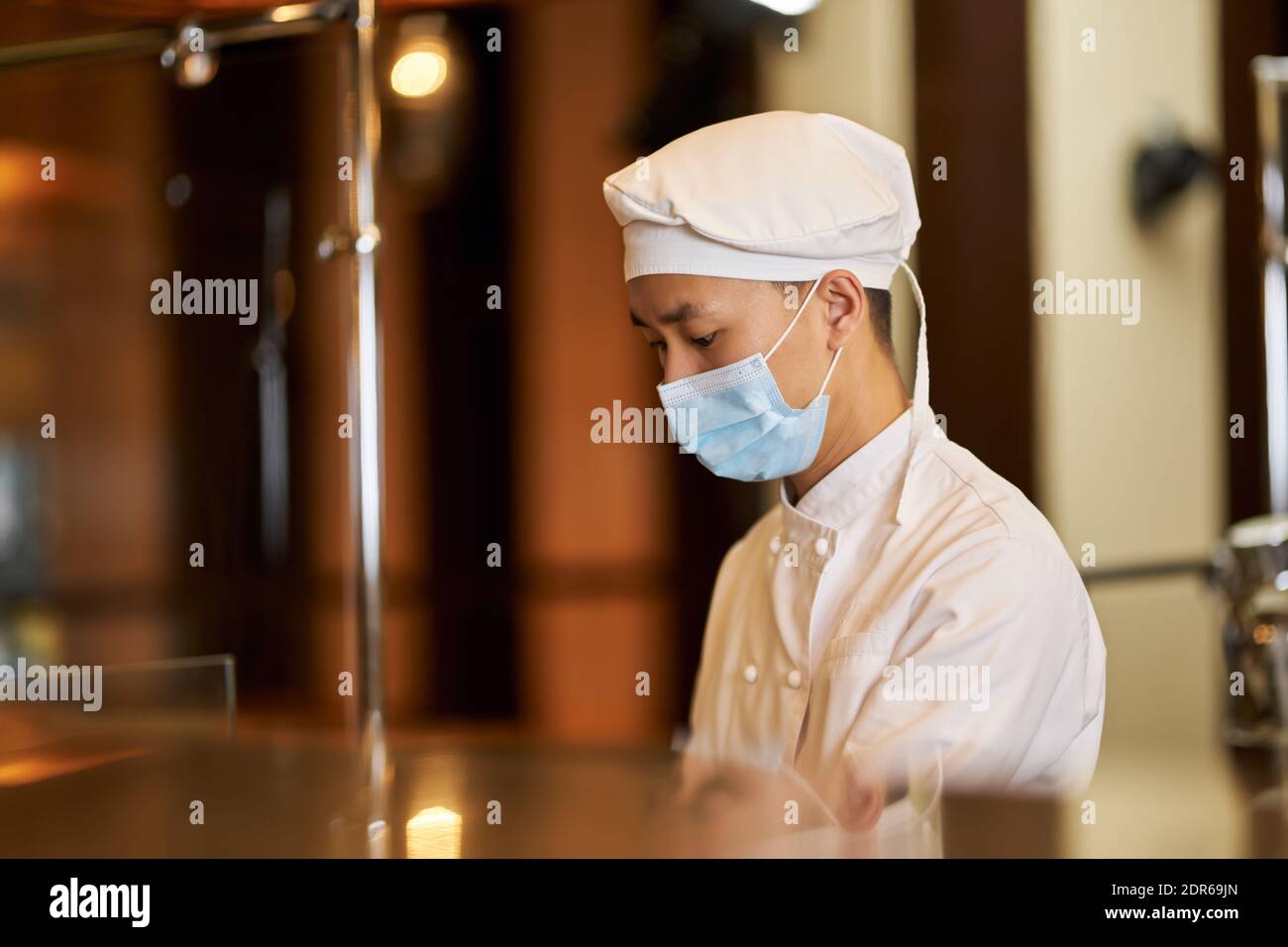 Seitenansicht Foto von aufmerksamen jungen Koch trägt Gesichtsmaske während Sich auf seine Arbeit konzentrieren Stockfoto