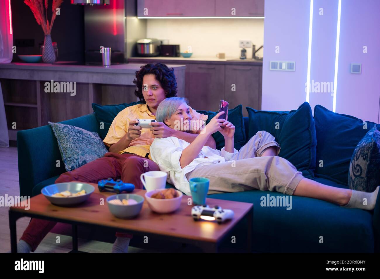 Glückliches junges Paar, das ein Videospiel spielt, das zu Hause auf einem Sofa während der Selbstisolierung in Quarantäne sitzt. Stockfoto
