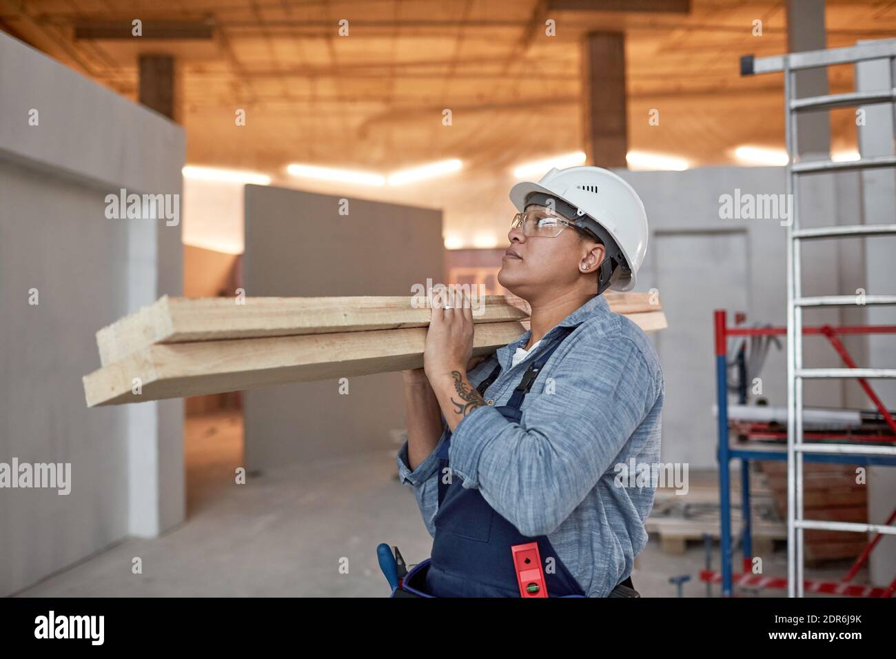 Waist up Porträt der modernen Arbeiterin trägt Holzbretter während der Arbeit auf der Baustelle, kopieren Raum Stockfoto