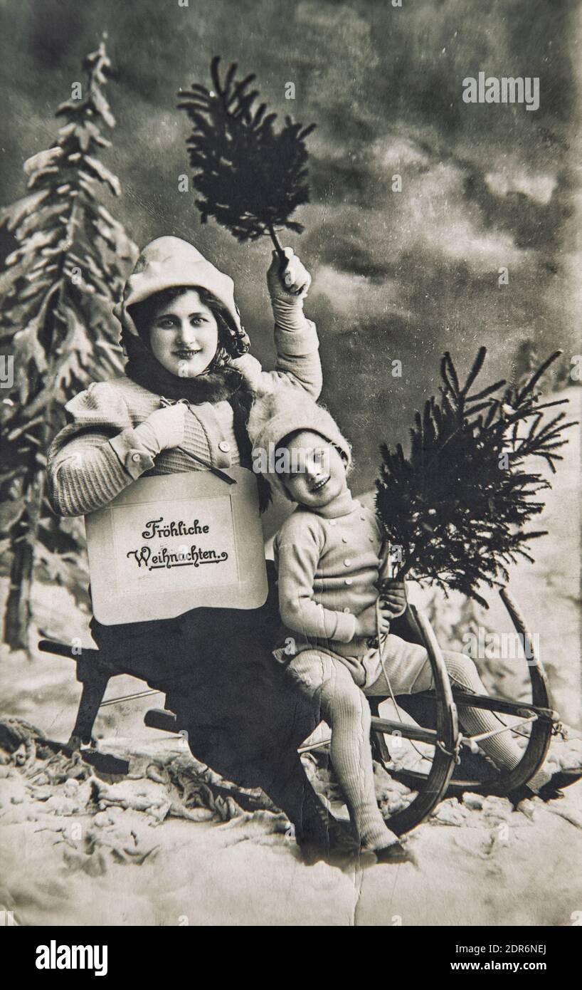 Mutter und kleiner Junge mit Schlitten, Geschenke, Weihnachtsbaum. Alte deutsche Postkarte mit original Film Maserung und Kratzern Stockfoto