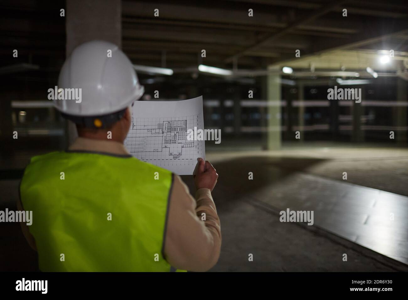 Rückansicht einer Ingenieurin, die Baupläne hält, während sie die Basis des Gebäudes auf der Baustelle inspiziert, Platz kopieren Stockfoto