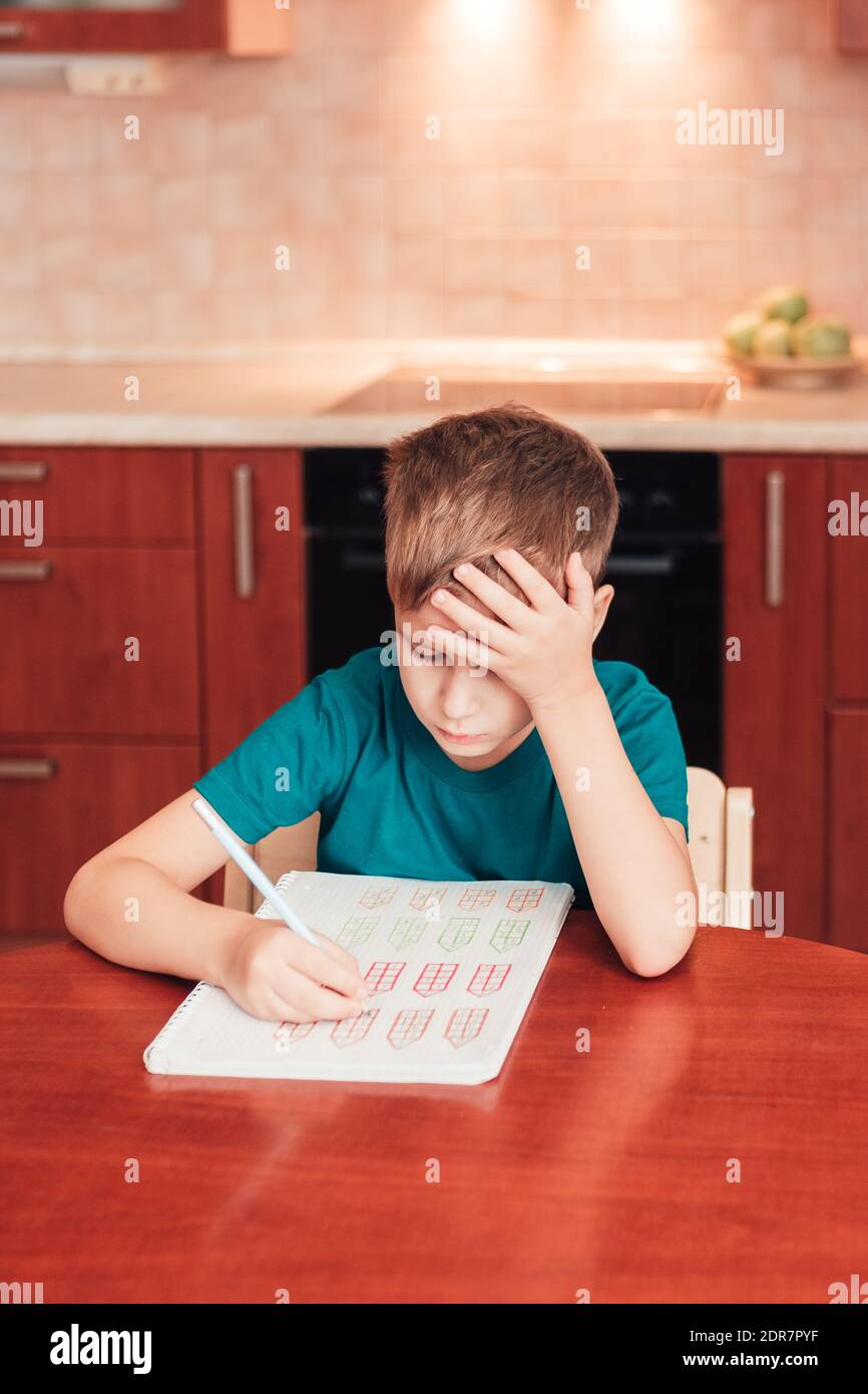 7 yeas altes Kind sitzt am Tisch in der Küche und macht Mathe-Übung, schwierige Hausaufgaben, Kind konzentriert sich auf Beispiele Stockfoto