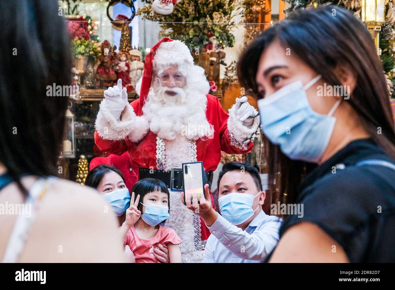 Menschen mit Gesichtsmasken fotografieren mit dem Weihnachtsmann im Pavillion Einkaufszentrum in Kuala Lumpur. Stockfoto