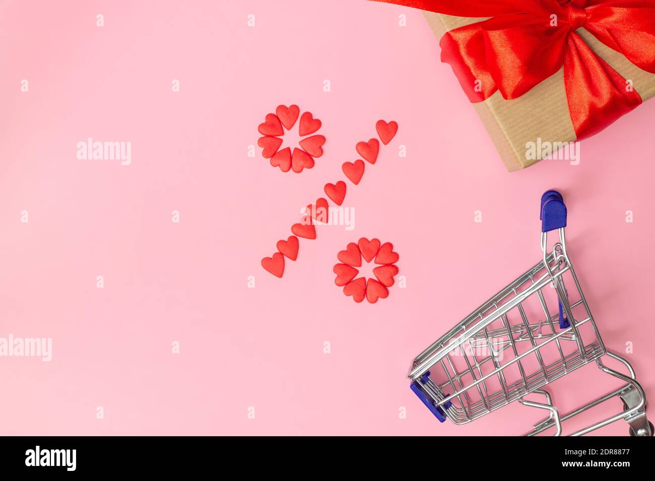 Prozent Zeichen mit kleinen roten Herzen mit Geschenk in gefüttert Basteln Sie Papier und Band und Warenkorb auf rosa Hintergrund Stockfoto