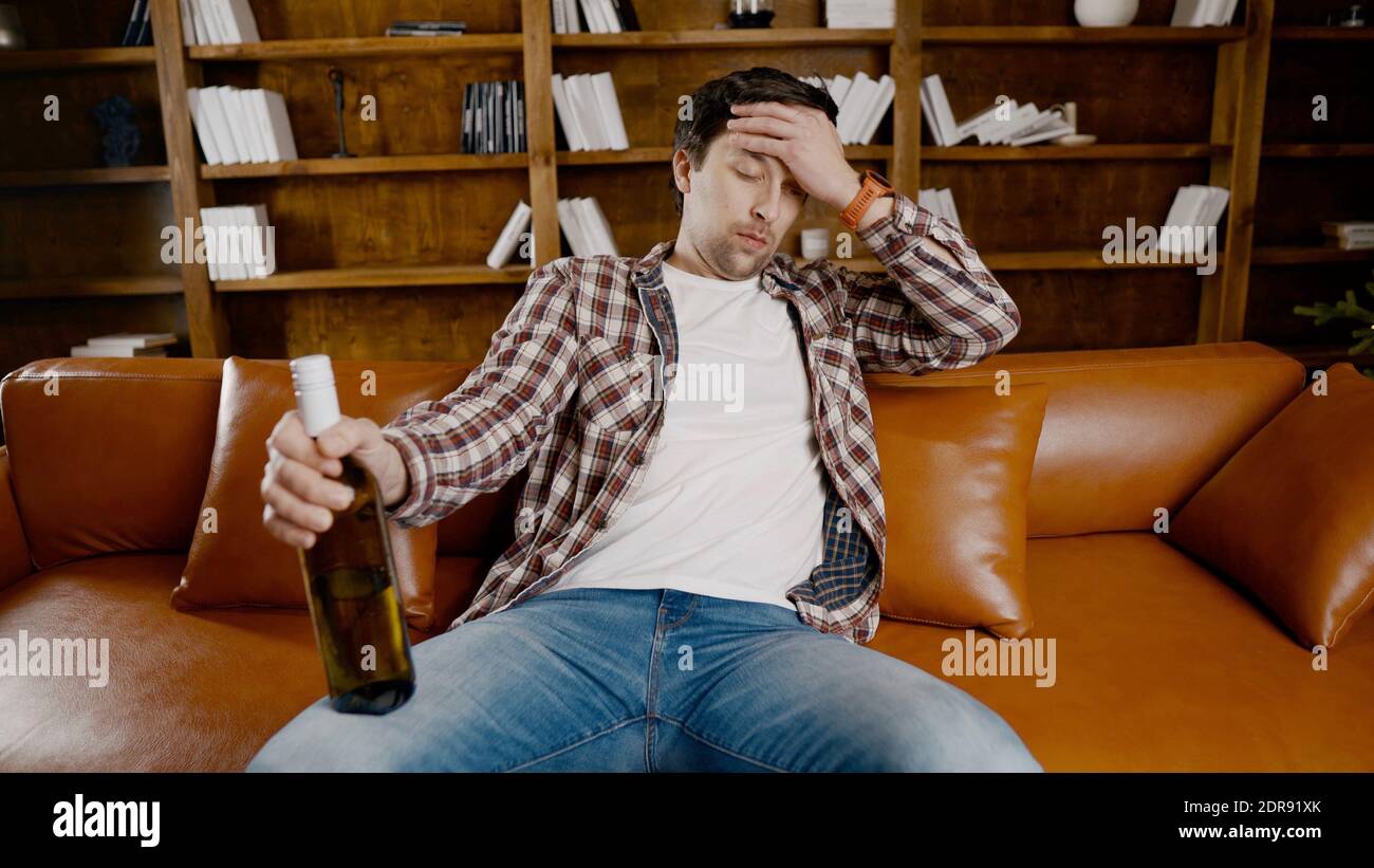 Deprimierter junger Mann, der zu Hause Alkohol trinkt. Arbeitslos männlich,  betrunken und weiter trinken Wein gerade Flasche auf der Couch in der Nähe  von Weihnachtsbaum. Sucht Stockfotografie - Alamy