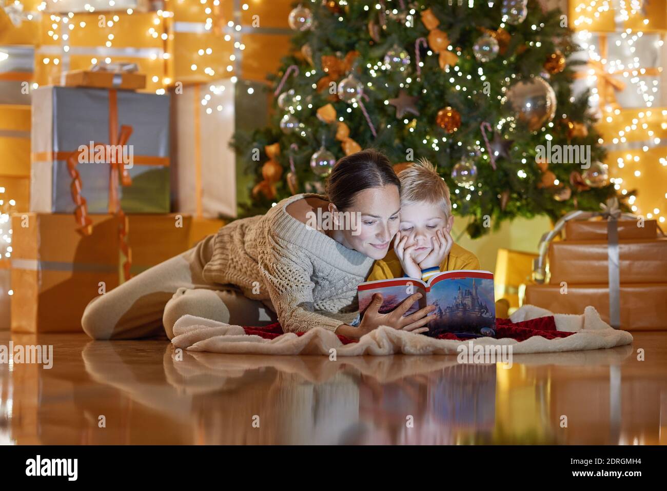 Mutter liest ihr Sohn Buch unter dem Weihnachtsbaum Stockfoto