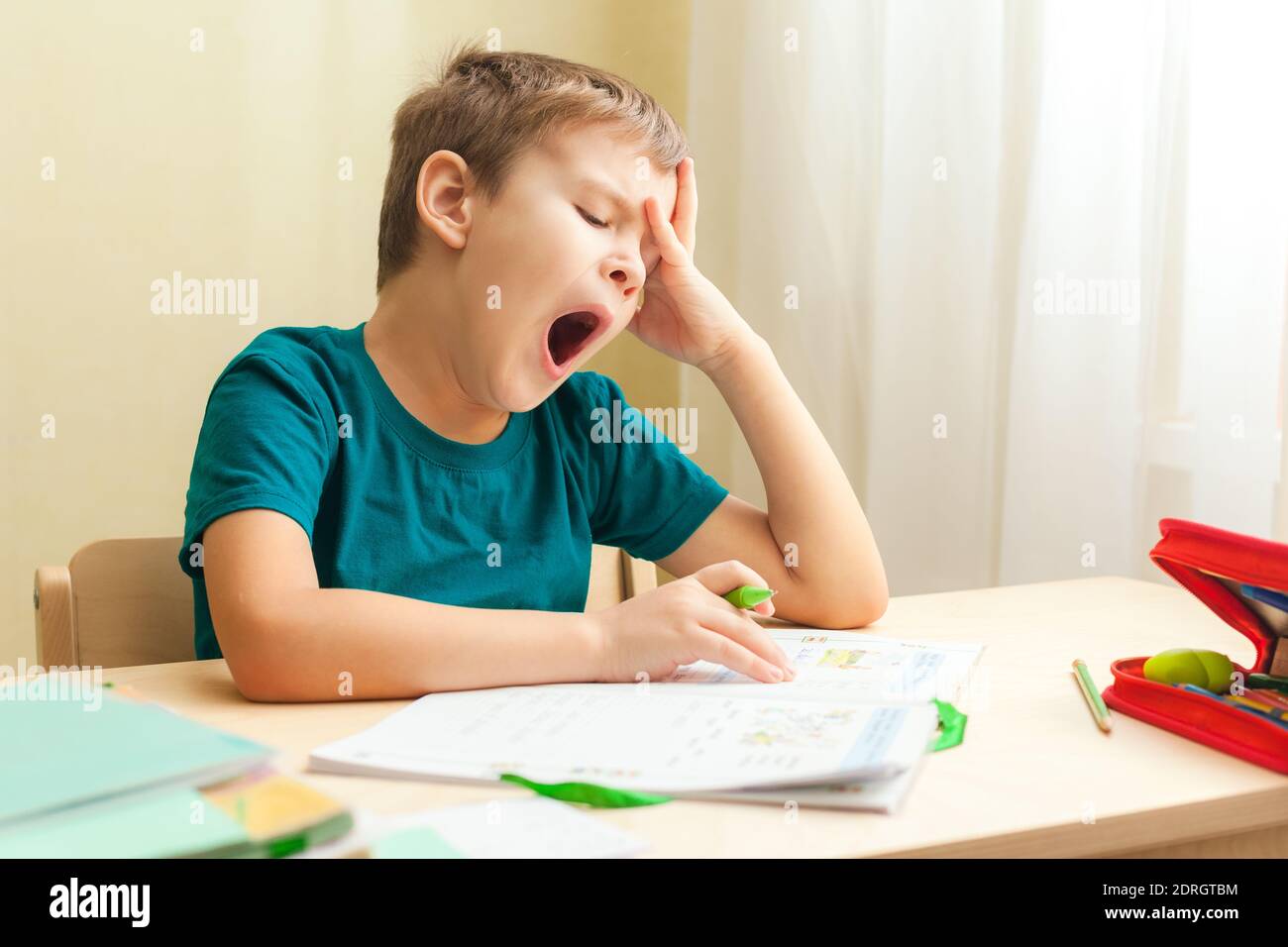 7 Jahre alter Junge, der am Schreibtisch sitzt und Hausaufgaben macht. Kind schreibt Notizen im Notizbuch, schwierige Hausaufgaben, Kind konzentriert sich auf Beispiele Stockfoto
