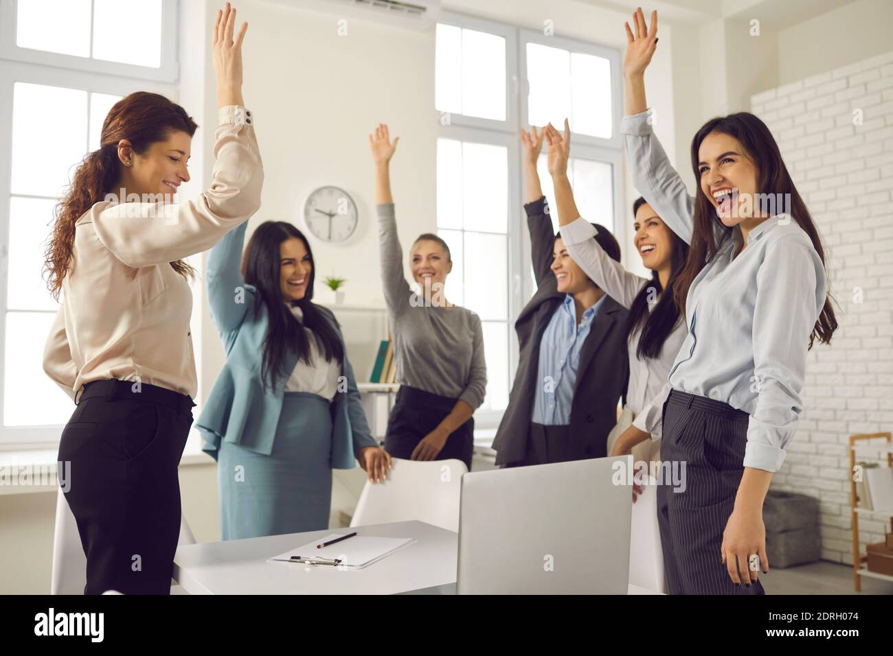 Gruppe von glücklichen Frauen, die die Hände heben und für eine gute Idee in einem Unternehmensmeeting stimmen Stockfoto