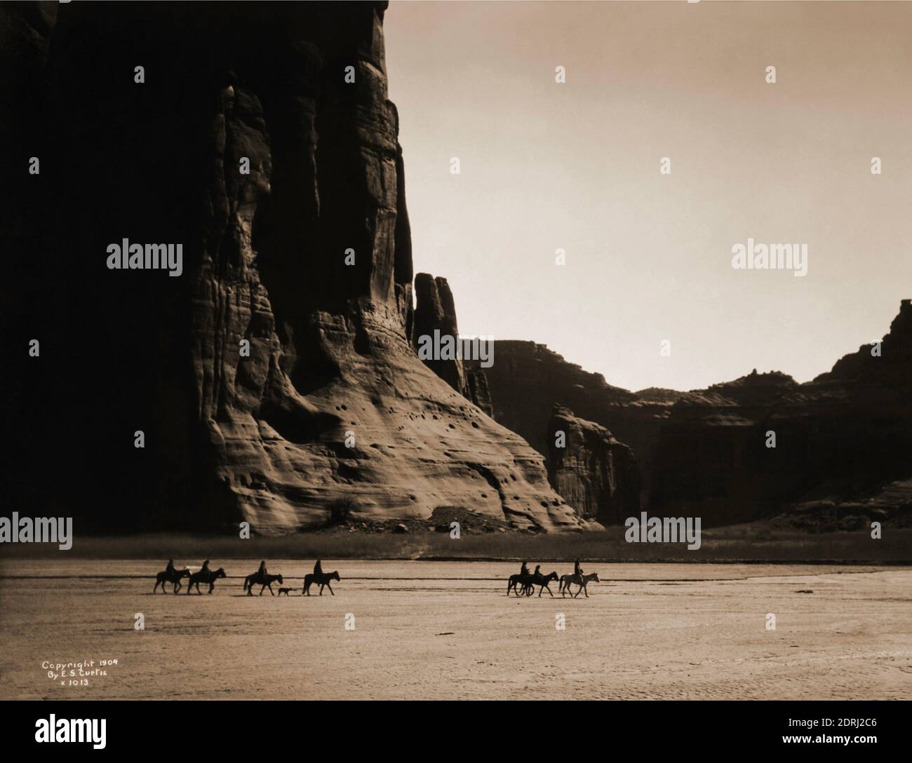 Vintage-Foto von 1904 von Edward S Curtis von sieben Reitern auf dem Pferd und Hund Trekking vor dem Hintergrund der Canyon Klippen. Canyon De Chelly. Stockfoto