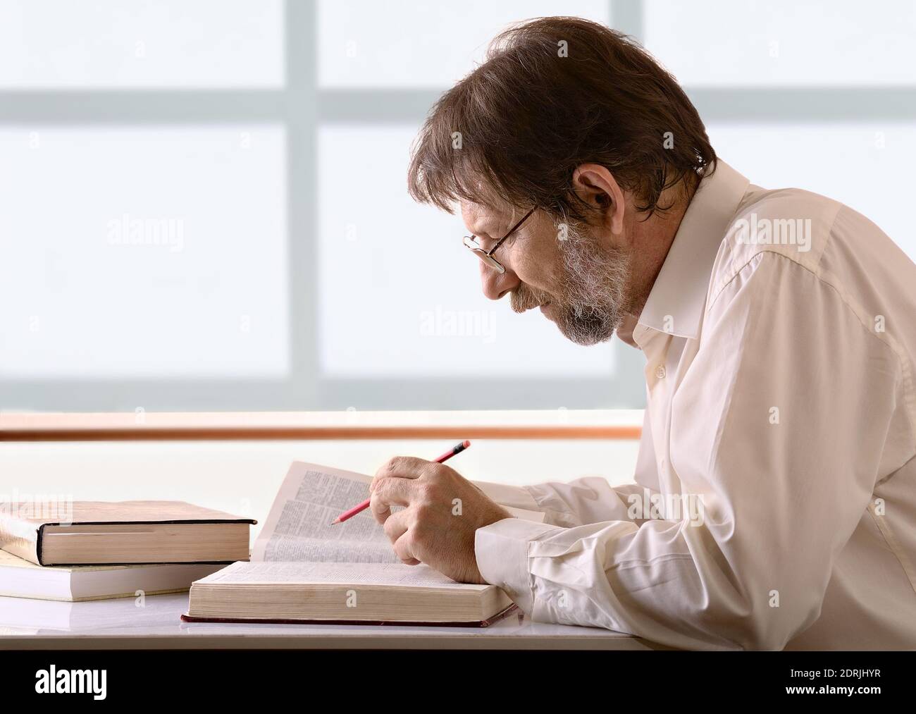 Älterer Mann mit einem Bleistift in der Hand sitzend Ihr Schreibtisch Stockfoto