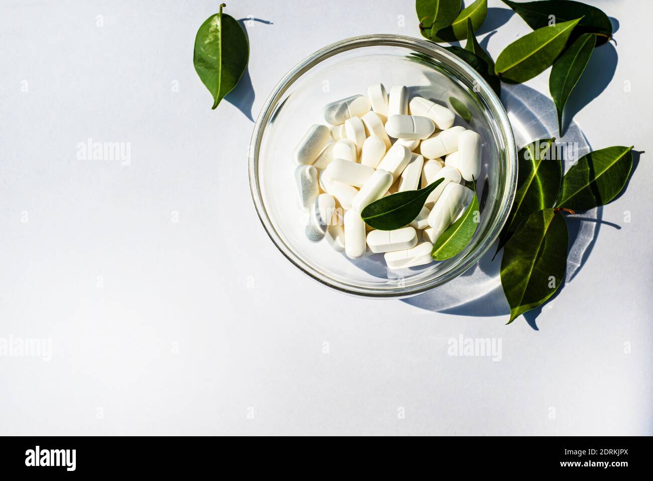 Kapseln Vitamine und Mineralstoffe in einer Glasschale und eine Streuung von grünen Blättern auf weißem Hintergrund. Platz für Text kopieren Stockfoto