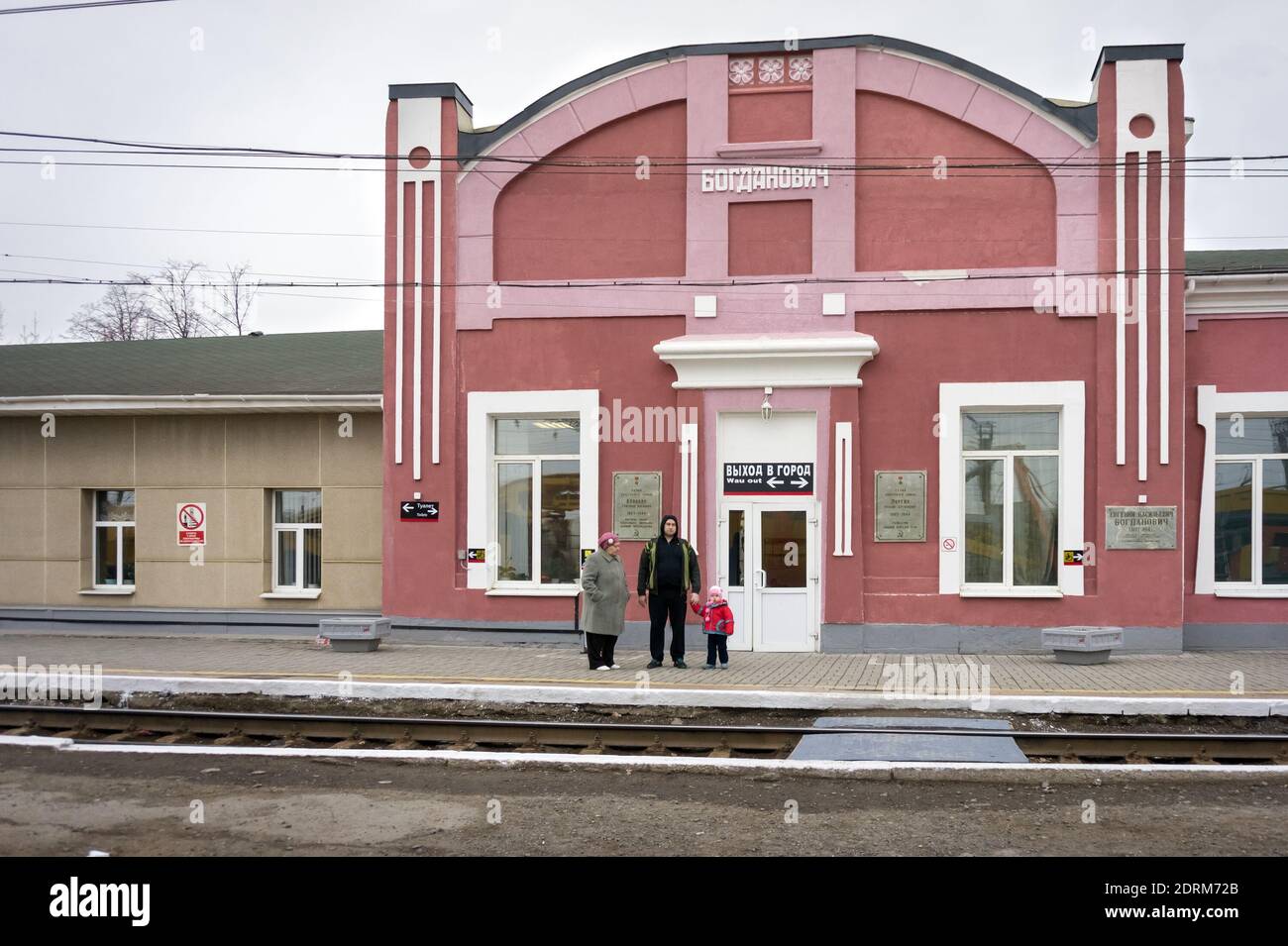 An einem bewölkten Frühlingstag stehen die Menschen auf dem Bahnsteig in der Nähe des alten Gebäudes des Bahnhofs (1885) in der Stadt Bogdanovich. Stockfoto